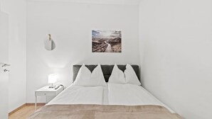 A bedroom with a bed, a nightstand, a lamp, a wall-mounted toilet, and a picture of a landscape. - FarawayHomes Studio Mürzzuschlag #4 (Mürzzuschlag)