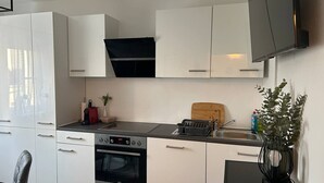 Moderni keittiö, jossa on valkoiset kaapit, sisäänrakennettu uuni, liesi ja musta työtaso.