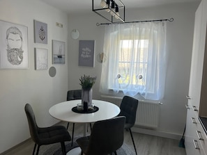 Ein Essbereich mit einem runden Tisch, vier Stühlen, einer Blumenvase und einem Fenster mit durchsichtigen Vorhängen.