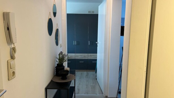 Kapea käytävä johtaa moderniin keittiöön, jossa on tummat kaapit ja vaaleansävyinen lattia.