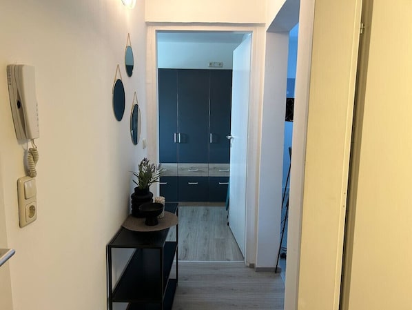 A narrow hallway leading to a modern kitchen with dark cabinets and a light-colored floor.