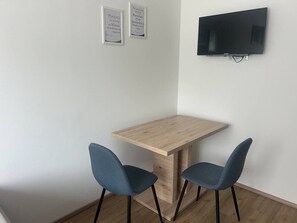 Ett litet rum med ett träbord och två stolar, en platt-TV som är monterad på väggen och två inramade citat på väggen.