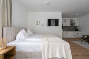 A modern hotel room with a bed, a TV, a kitchenette, and a wooden side table. - FarawayHomes Studio Fohnsdorf #A1 (Fohnsdorf)