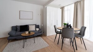 Una sala de estar moderna con un sofá gris, una mesa redonda con sillas, un tapete pequeño y un cuadro enmarcado en la pared.