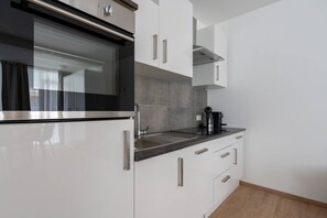 A modern kitchen with white cabinetry, a black oven, and a coffee maker on the countertop. - FarawayHomes Studio Fohnsdorf #A1 (Fohnsdorf)