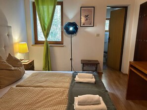 Un dormitorio con cama, lámpara de noche, lámpara de pie, ventana con cortinas, un cuadro enmarcado en la pared y una puerta de madera.