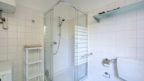 Un bagno con cabina doccia in vetro, lavandino bianco e ripiano con asciugamani.