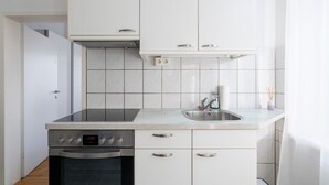 Una cucina compatta con pensili bianchi, un lavello in acciaio inox e una sveglia digitale.