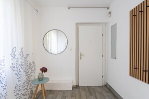 A hallway with a white door, a round mirror, a small table with a vase, and a wooden panel on the wall. - FarawayHomes Studio Klosterneuburg #2 (Klosterneuburg)