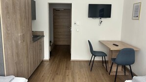 Une chambre moderne avec un plancher en bois, un bureau avec deux chaises, une télévision et une porte donnant sur une autre pièce.