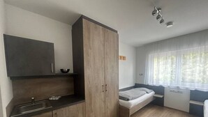 Quarto compacto com cozinha compacta, uma cama e uma janela com cortinas leves.