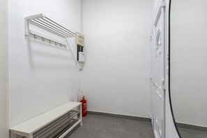 Une petite pièce propre, avec un banc blanc, un extincteur, une boîte électrique fixée au mur et une porte.
