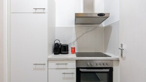 A compact kitchen with a built-in oven, a coffee maker, and a kettle on the countertop.