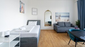 A modern hotel room with a bed, a sofa, a dining table, and a mirror.