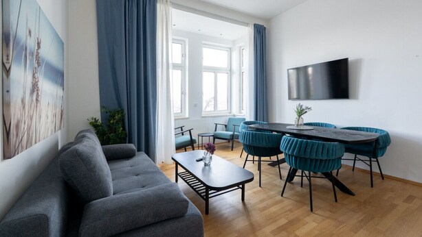 A modern living room with a sofa, dining table, chairs, and a TV.
