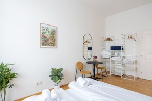 Une chambre d’hôtel avec un lit, un bureau, une chaise, un miroir, une plante, une armoire et un tableau au mur.