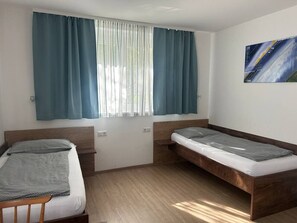 Una habitación con dos camas, una ventana con cortinas, un cuadro en la pared y suelo de madera.