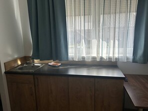 Ett kök med en diskho, träskåp, ett fönster med tunna gardiner och utsikt över omgivningen.