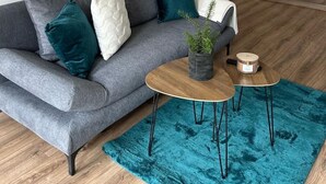 A grey sofa with teal and white cushions, a small round table with a plant and a candle, and a blue rug on a wooden floor. - FarawayHomes Studio Bruck #5 (Bruck an der Mur)