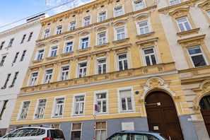 Ein mehrstöckiges Gebäude mit gelber Fassade, großen Fenstern und einem markanten Eingang.
