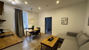 Una sala de estar moderna con sofá, una mesa de comedor con sillas, un área de cocina con fregadero y una ventana con cortinas.
