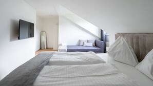 Un dormitorio moderno con una cama grande, una cama más pequeña, un televisor y un ventanal amplio.