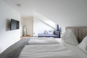 A modern bedroom with a large bed, a smaller bed, a TV, and a large window.