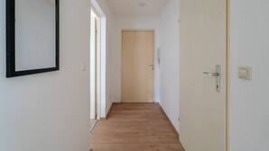 Un pasillo estrecho con suelo de madera, paredes blancas y una puerta al final.