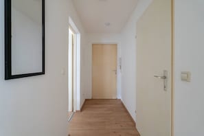A narrow hallway with wooden flooring, white walls, and a door at the end.