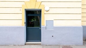 Un edificio con una puerta azul oscuro, una ventana pequeña y una caja de servicios a un lado.