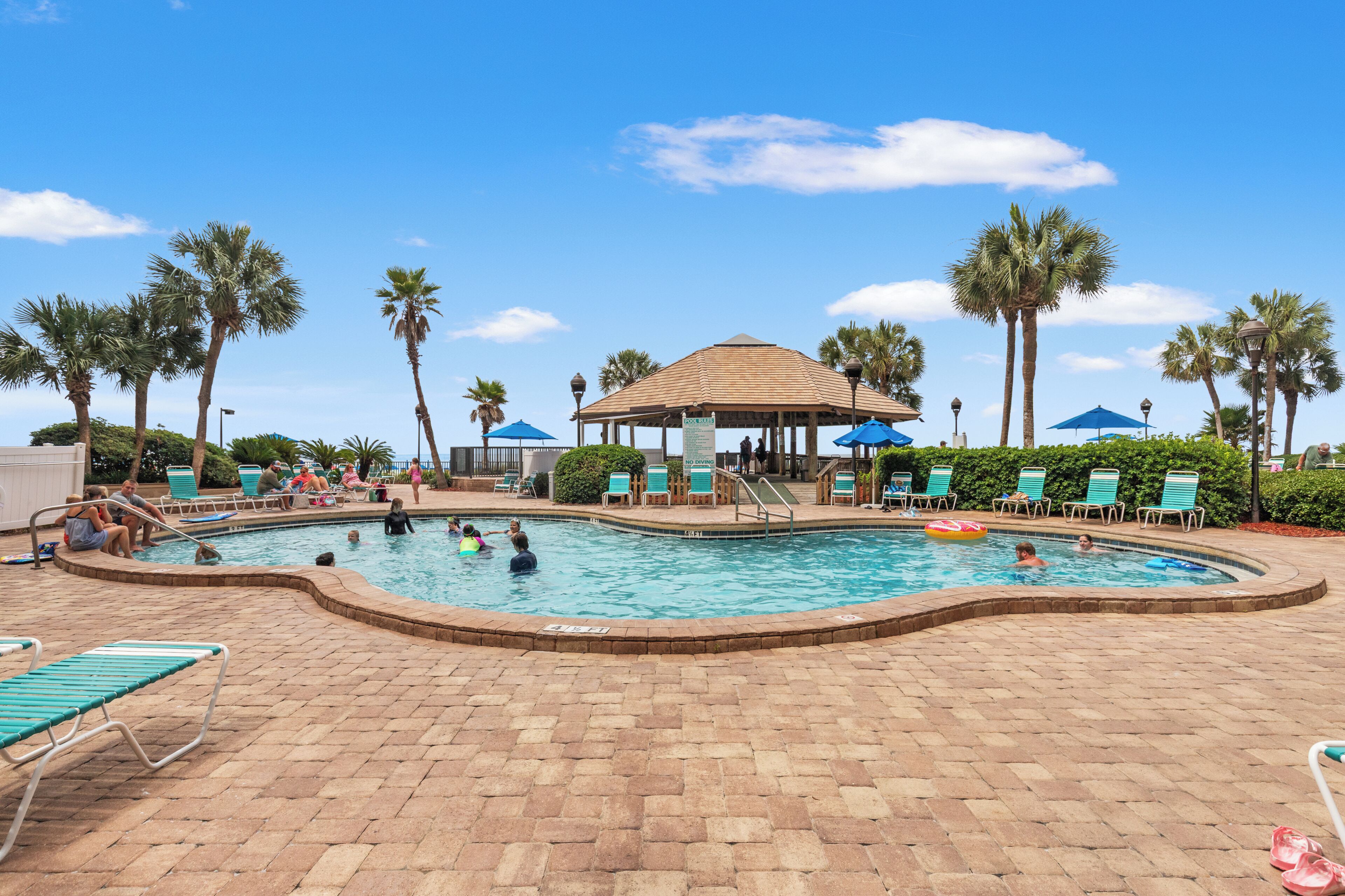 A swimming pool area with lounge chairs, palm trees, and a gazebo.