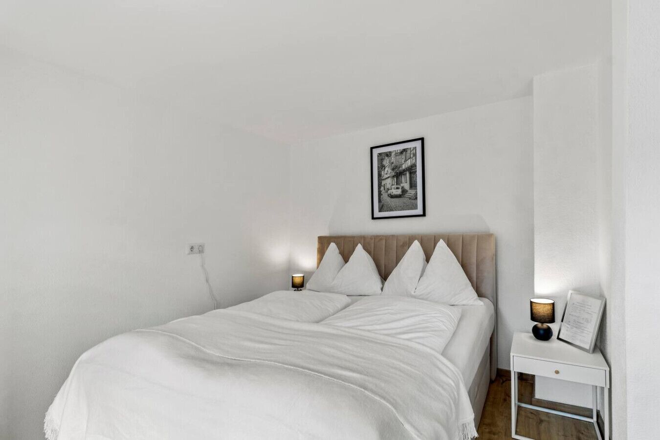 Ein Schlafzimmer mit einem Bett, zwei Nachttischen, einer Steckdose und einem gerahmten Bild an der Wand.