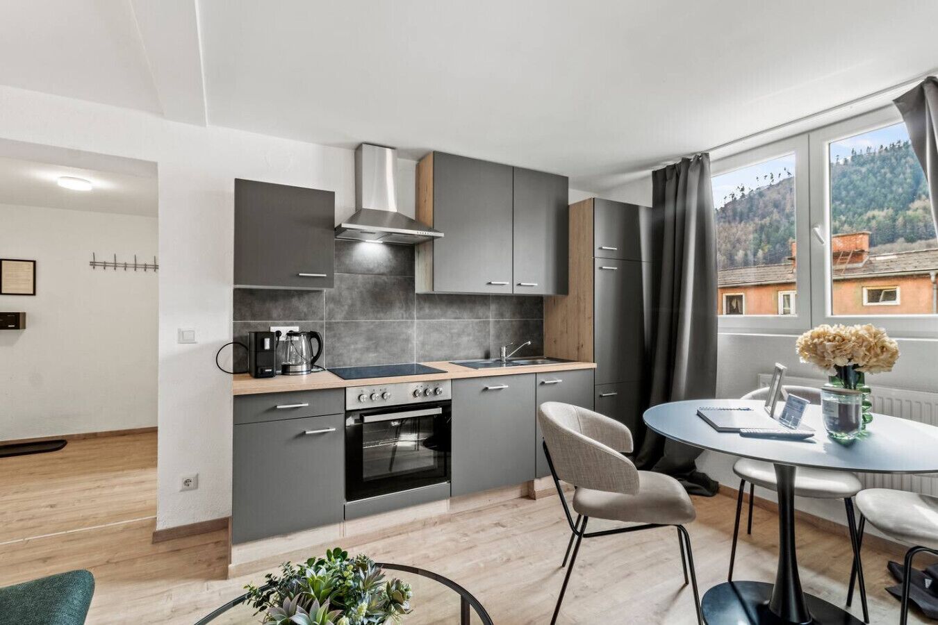 Une cuisine moderne avec des meubles gris, une cuisinière et un évier. On y trouve également un coin repas avec une table ronde et deux chaises.