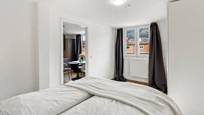 A bedroom with a bed, a window with curtains, a radiator, and a view of buildings outside. - FarawayHomes Studio Leoben #P81 (Donawitz)