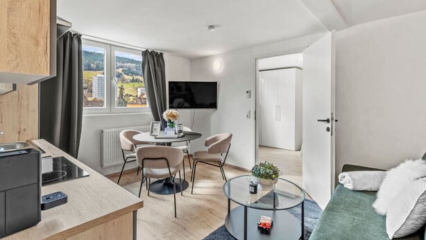A modern kitchen with a dining area, a TV, and a view of a cityscape. - FarawayHomes Studio Leoben #P81 (Donawitz)