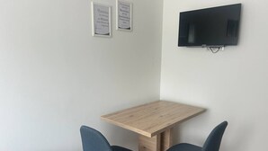 A small room with a wooden table and two chairs, a flat-screen TV mounted on the wall, and two framed quotes on the wall. - FarawayHomes Aparthotel Kremsmünster #14 (Kremsmünster)