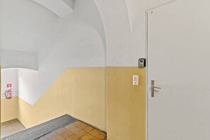 A hallway with a white door, a fire alarm, and a light switch on the wall. - FarawayHomes Studio Leoben #K7 (Donawitz)