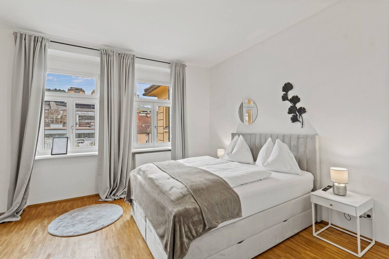 A bedroom with a bed, a bedside table, a round rug, and a window with curtains.. FarawayHomes Studio Leoben #K7