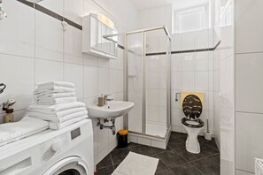 A modern bathroom with a washing machine, stacked towels, a sink, a toilet, and a glass shower enclosure. - FarawayHomes Studio Leoben #K7 (Donawitz)