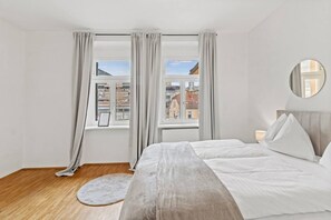 A bedroom with a bed, a round mirror, and a view of buildings through large windows. - FarawayHomes Studio Leoben #K7 (Donawitz)