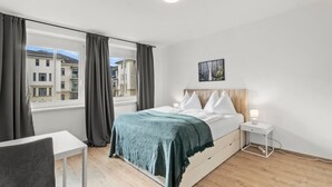 A bedroom with a bed, bedside table, and a view of buildings through a window. - FarawayHomes Studio Leoben #A5 (Leitendorf)
