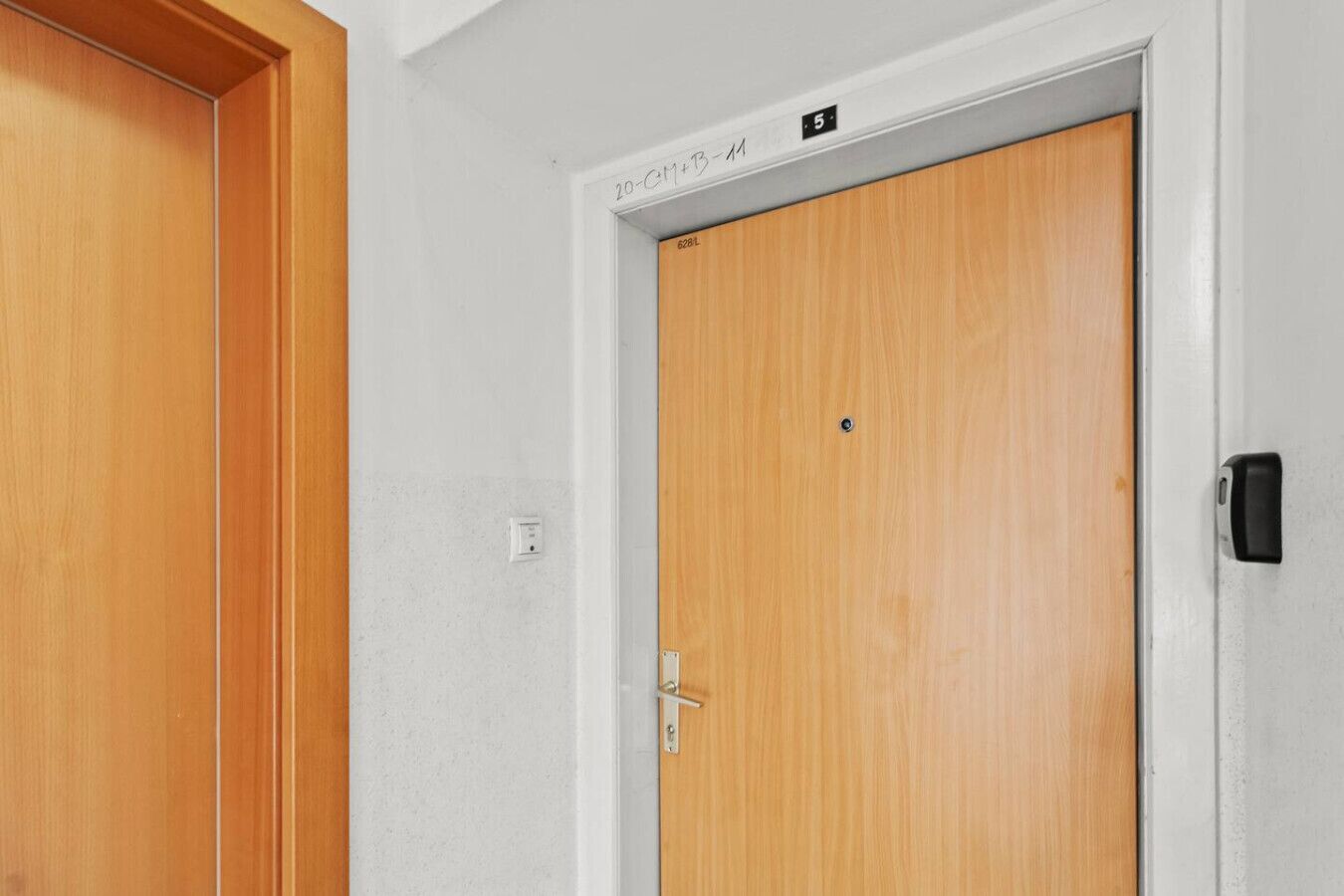 Una porta de fusta amb una manilla metàl·lica, una paret blanca i un petit objecte negre a la porta.