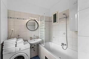 Een badkamer met een wasmachine, wastafel, spiegel en bad.