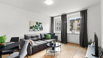 Een moderne woonkamer met een grijze bank, een ronde salontafel en een eethoek met een tafel en stoelen.