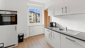 A modern kitchen with a built-in oven, a window with a view of buildings, a sink, and cabinets. - FarawayHomes Studio Leoben #A5 (Leitendorf)