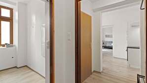 Un interior moderno con un marco de puerta de madera, una zona de cocina con encimera gris y una ventana visible con una planta en el alféizar.