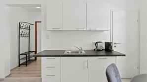 Cocina compacta con armarios blancos, encimera negra, hervidor y cafetera.