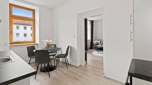 Una cocina moderna con comedor, un ventanal con vistas a edificios y un pasillo que conduce a una sala de estar.