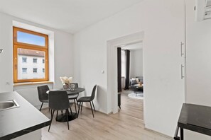 Een moderne keuken met een eethoek, een raam met uitzicht op gebouwen, en een gang die leidt naar een woonruimte.