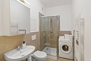 Ein modernes Badezimmer mit einer Duschkabine, einem Waschbecken, einer Toilette und einer integrierten Waschmaschine.